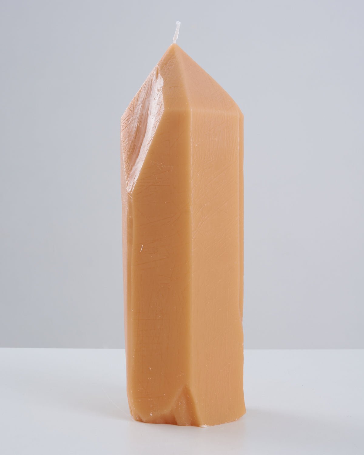 Vela Citrino artesanal na cor caramelo, em formato de ponta de cristal facetada com topo em bico, isolada sobre superfície branca com fundo claro