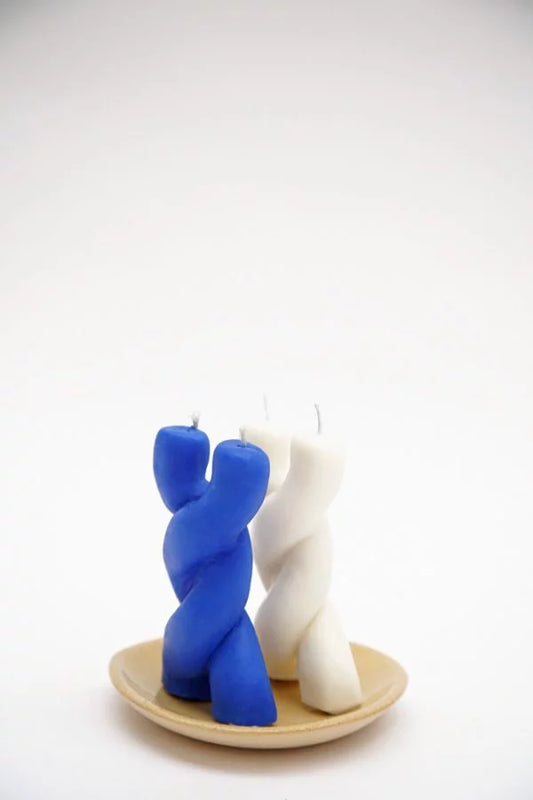 Duas velas Encontro artesanais, azul e branca, sobre pratinho de cerâmica